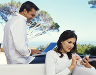 man working on a laptop and a woman using her mobile phone outside